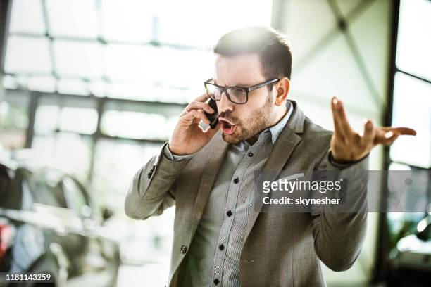 uomo d'affari arrabbiato che parla al cellulare in uno showroom di auto. - rabbia emozione negativa foto e immagini stock