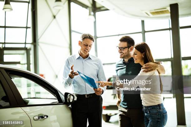 feliz pareja leyendo plan de compra con vendedor de coches en una sala de exposición. - comprar coche fotografías e imágenes de stock