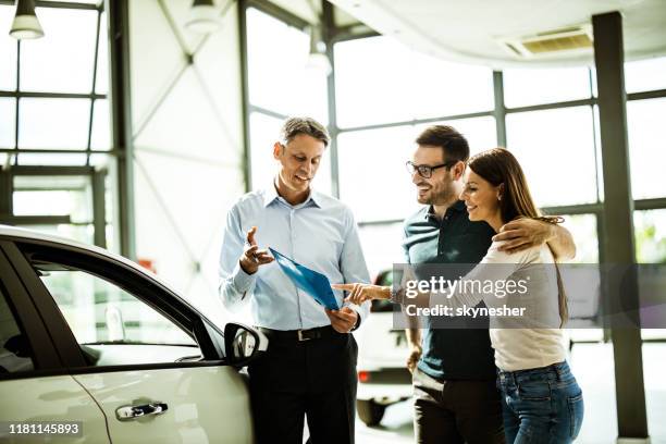 幸福的夫婦閱讀購買計畫與汽車銷售人員在展廳。 - buying a car 個照片及圖片檔