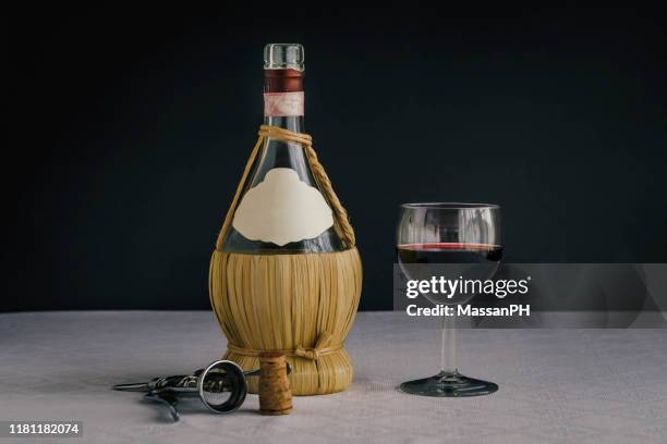 a flask of red wine on a white tablecloth and black background, next to a half-filled chalice, a corkscrew and a cork stopper - wine cork stockfoto's en -beelden