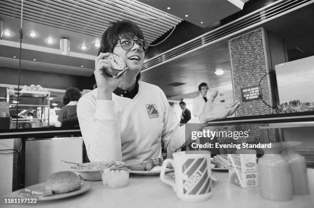 English radio DJ, writer, journalist and television presenter Mike Read holding a table clock at a cafe, UK, 19th November 1980.