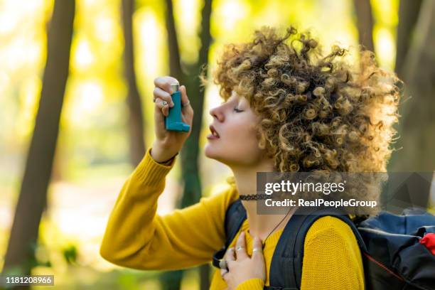 vrouw wandelaar met behulp van inhalator buiten in hout. jonge vrouw die astma behandelt met een inhalator - ladies of the real on extra stockfoto's en -beelden