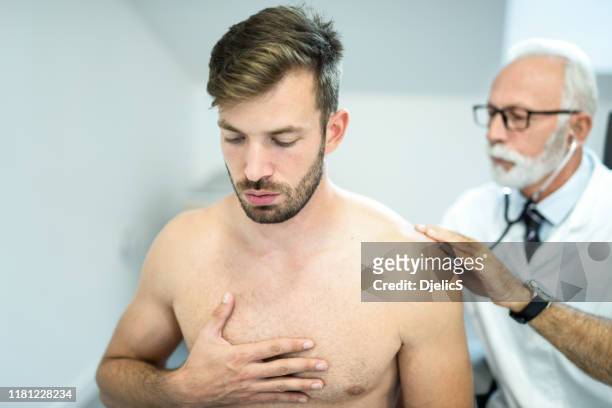 arzt untersucht die lunge des jungen mannes mit stethoskop. - herzton abhören stock-fotos und bilder