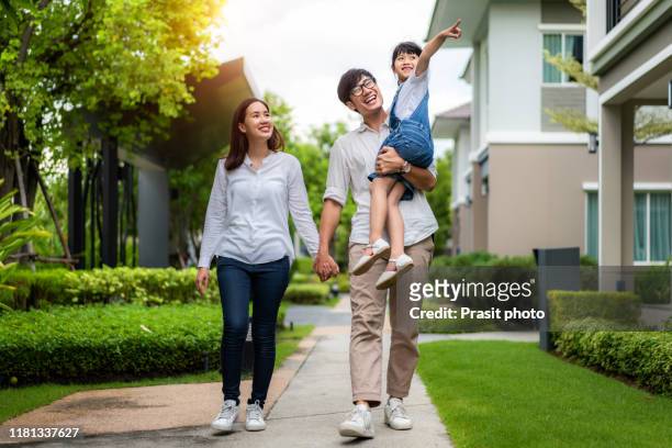 asian family portrait daughter, mother and father walking and point to their new house in village. she looking happy with new house in modern village. family life love relationship, or home fun leisure activity concept - happy family home outdoors stockfoto's en -beelden