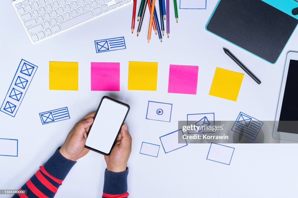 Ux designer hands holding white screen smartphone mockup on white office desk. User Experience Design Process concept.