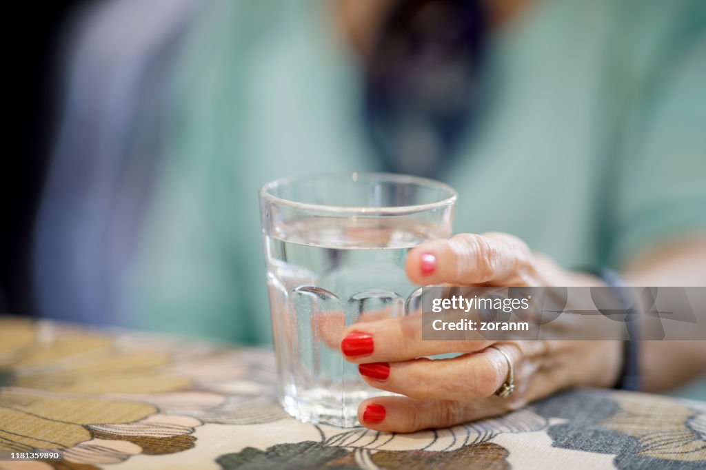 Wrinkled female hand holding glass of water