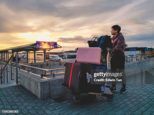 una mujer china asiática acaba de llegar al aeropuerto de keflavik esperando al aire libre con la puesta de sol hermosa con su equipaje - carrito-para-equipaje fotografías e imágenes de stock