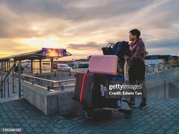 an asian chinese female just arrived at keflavik airport waiting outside with beautiful sunset with her luggage - luggage trolley stock pictures, royalty-free photos & images