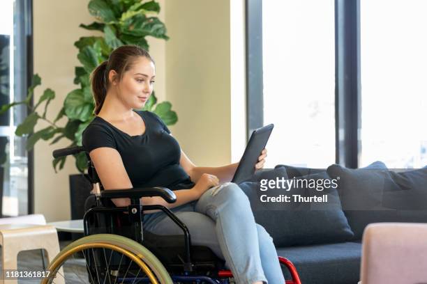 portrait of young woman with hidden illness in wheelchair using digital tablet - wheelchair access stock pictures, royalty-free photos & images