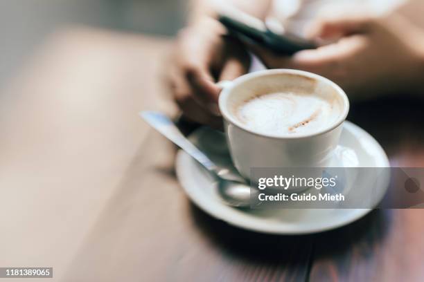 having a cup of coffee at a cafe while using mobile phone. - roma capucino stock pictures, royalty-free photos & images