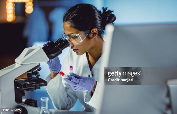 joven científico que mira a través de un microscopio - investigacion fotografías e imágenes de stock