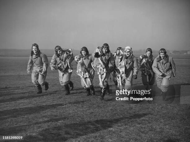 Group of eight female ferry pilots from the Air Transport Auxiliary , wearing full flight suits and parachutes, run towards their aircraft for...