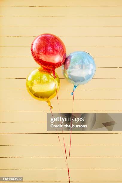 red, blue and gold colored helium balloons in front of yellow painted wooden wall - ballon de baudruche doré photos et images de collection