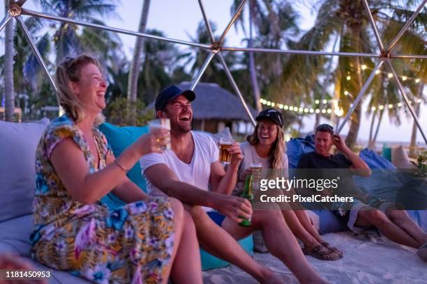 amici che ridono intorno al falò sulla spiaggia al tramonto - party sulla spiaggia foto e immagini stock