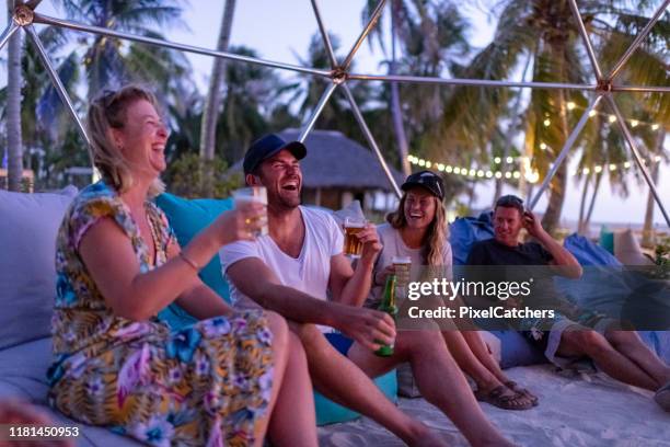 vrienden lachen rond het vreugdevuur op het strand bij zonsondergang - strandfeest stockfoto's en -beelden