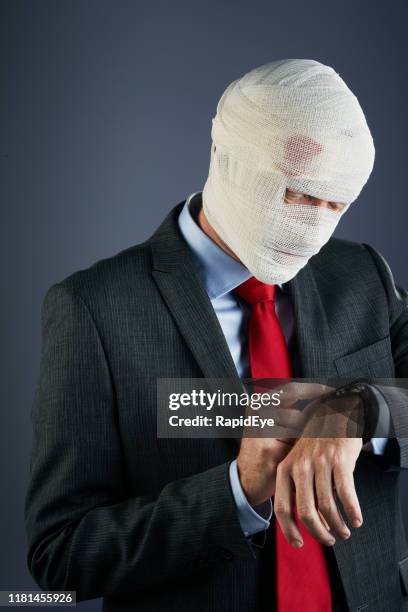 businessman wrapped in bandages checks the time on his watch - head bandage stock pictures, royalty-free photos & images