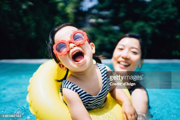 happy asian toddler girl with sunglasses smiling joyfully and enjoying family bonding time with mother having fun in the swimming pool in summer - divertirsi foto e immagini stock