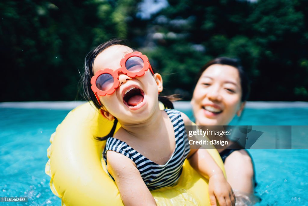 Happy Asian toddler girl with sunglasses smiling joyfully and enjoying family bonding time with mother having fun in the swimming pool in summer