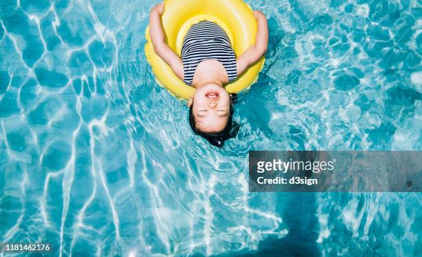 high angle view of cute asian toddler girl closed her eyes while floating with an inflatable ring relaxing at swimming pool - beach hotel imagens e fotografias de stock