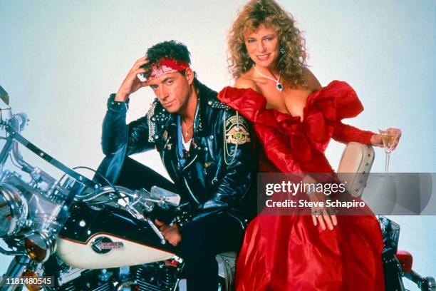 Portrait of American actor Ray Sharkey and English actress Jacqueline Bisset pose seated on a motorcycle and against a white background, in costume...