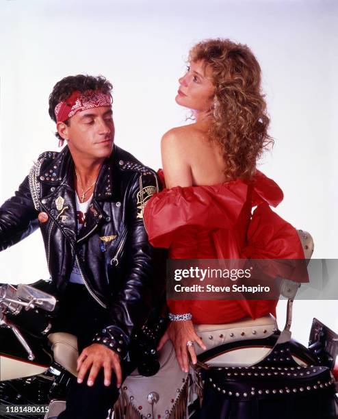 Portrait of American actor Ray Sharkey and English actress Jacqueline Bisset pose seated on a motorcycle and against a white background, in costume...