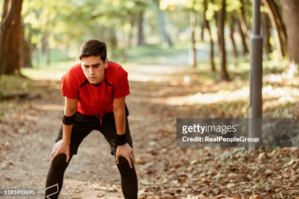 müde männliche jogger biegen im wald - atemlos stock-fotos und bilder