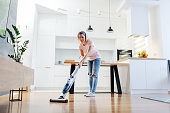 Full length of worthy caucasian blonde housewife using steamer to clean floor in living room.