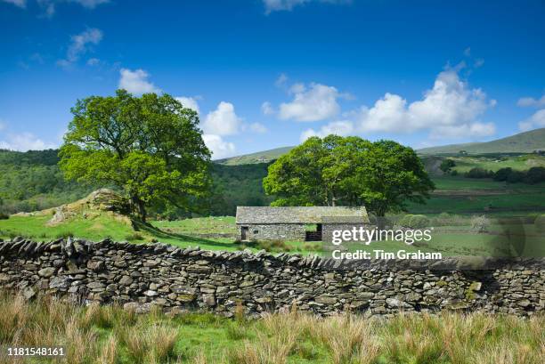 Stone barn and puffy clouds in blue sky near the River Duddon with Whitefell in the background in the Lake District, Cumbria, England.
