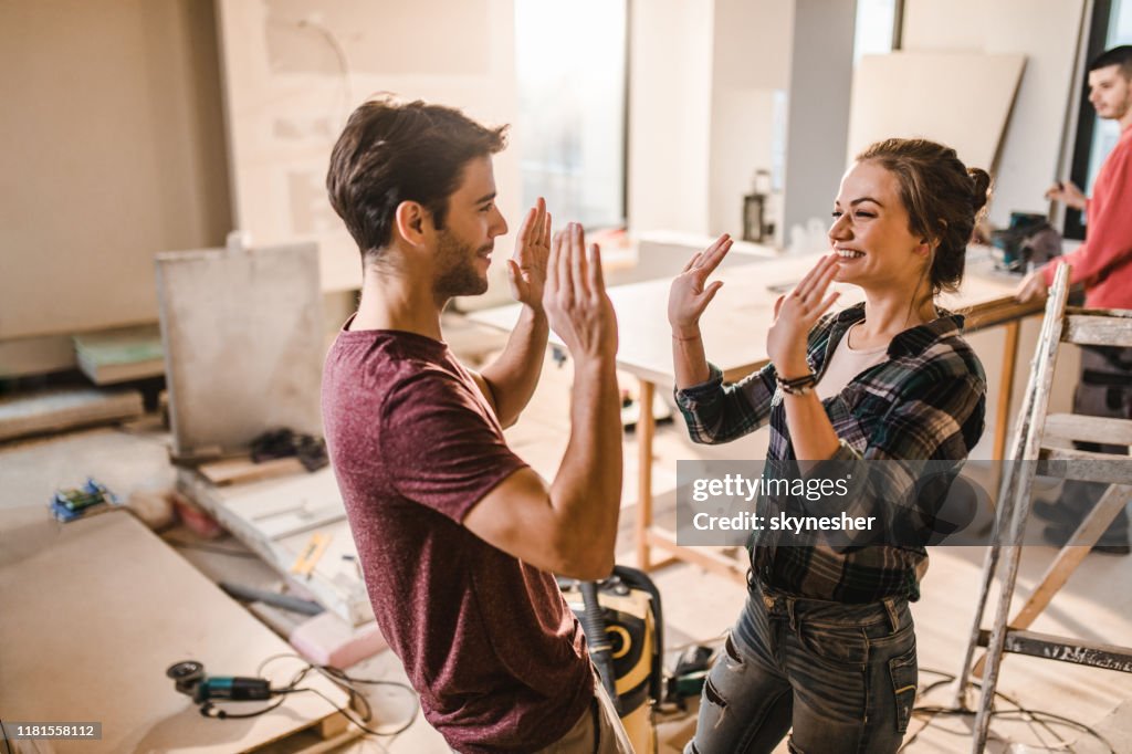 Pares felizes que dão um ao outro High-Five em seu apartamento renovar.