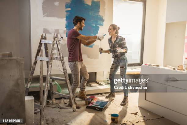 full length of happy couple having fun while painting their walls. - couple singing stock pictures, royalty-free photos & images