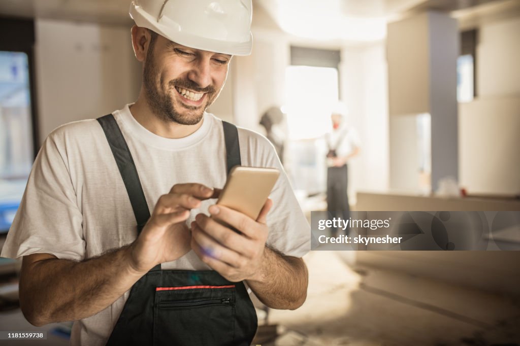 Happy construction worker using cell phone during home renovation.