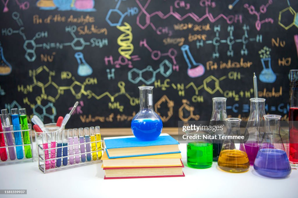 Classroom desk and drawn formula on blackboard of chemistry teaching with books and instruments.