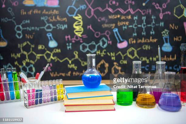 classroom desk and drawn formula on blackboard of chemistry teaching with books and instruments. - chemistry stock pictures, royalty-free photos & images