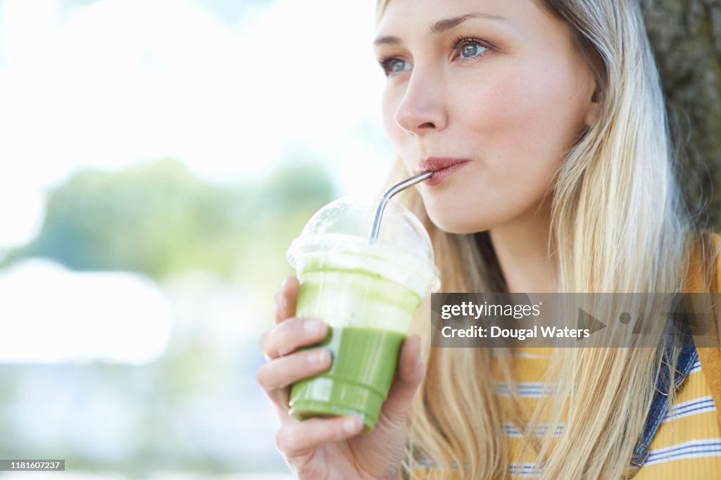 Young woman drinking fruit smoothie from plastic free compostable cup outdoors.