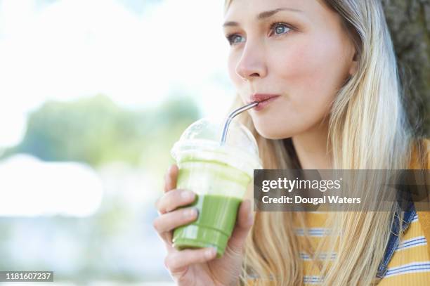 young woman drinking fruit smoothie from plastic free compostable cup outdoors. - metal straw stock pictures, royalty-free photos & images