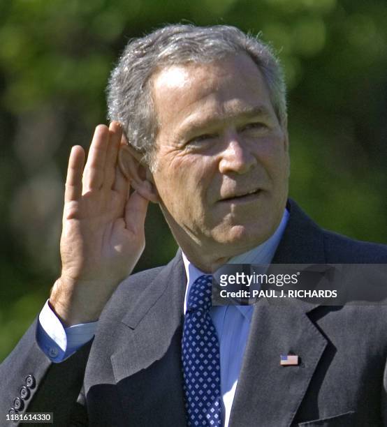 President George W. Bush puts his hand to his ear to indicate he can't hear the questions of reporters, as the engines of Marine One helicopter...