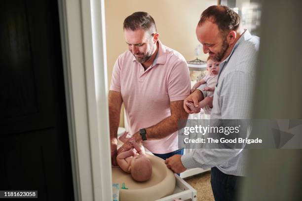 two fathers dressing baby girl in nursery - changing nappy stock pictures, royalty-free photos & images