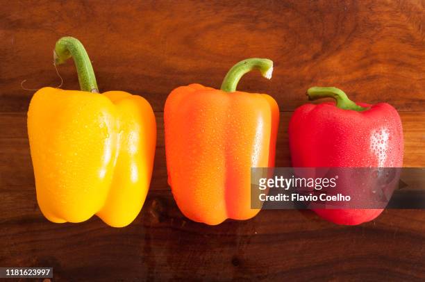 yellow, orange and red bell peppers on cutting board - orange bell pepper fotografías e imágenes de stock