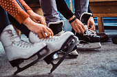 Young couple preparing to a skating. Close-up photo of their hands tying shoelaces of ice hockey skates in the locker room