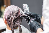 Close up of hairdresser hands is coloring woman's hair in black gloves.