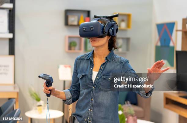 latin american woman at home having fun with a virtual realit headset and joystick - joystick stock pictures, royalty-free photos & images