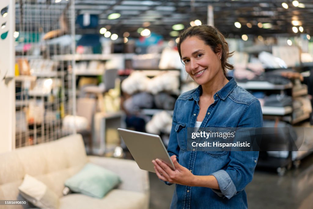Concepteur d'intérieur heureux à un magasin de meubles à la maison retenant une tablette tout en souriant à l'appareil-photo