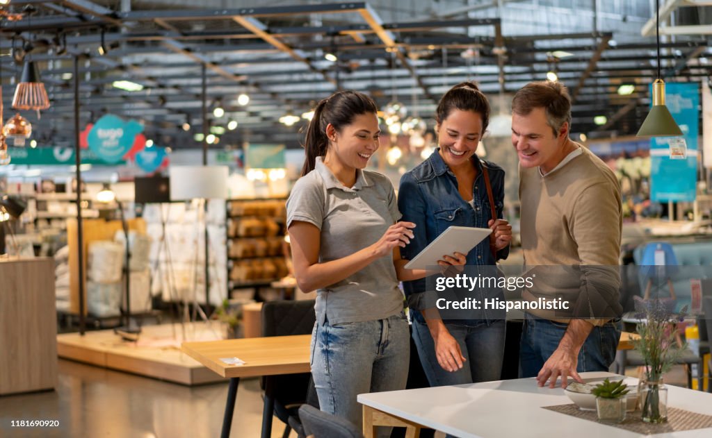 Fröhliche Verkäuferin zeigt ein Design auf Tablet zu mittleren erwachsenen Paar auf der Suche nach Möbeln in einem Home-Store