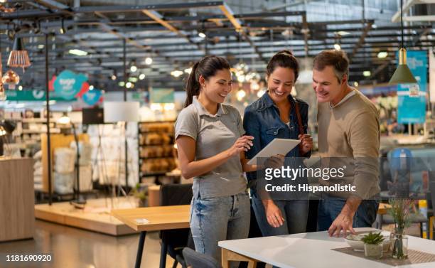 vrolijke verkoop vrouw die een ontwerp toont op tablet tot mid adult couple op zoek naar meubels in een thuiswinkel - shop stockfoto's en -beelden