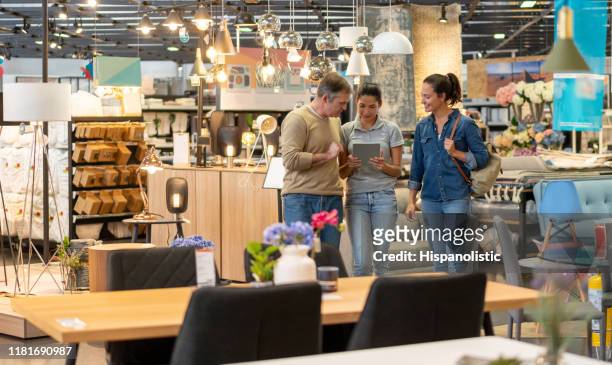 happy mid adult couple walking with sales woman at a furniture store choosing products and making the order on tablet - mid adult couple stock pictures, royalty-free photos & images