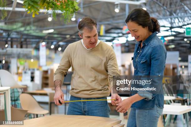latin american mid adult couple measuring a dining table at a furniture store talking and smiling - measuring potential business stock pictures, royalty-free photos & images