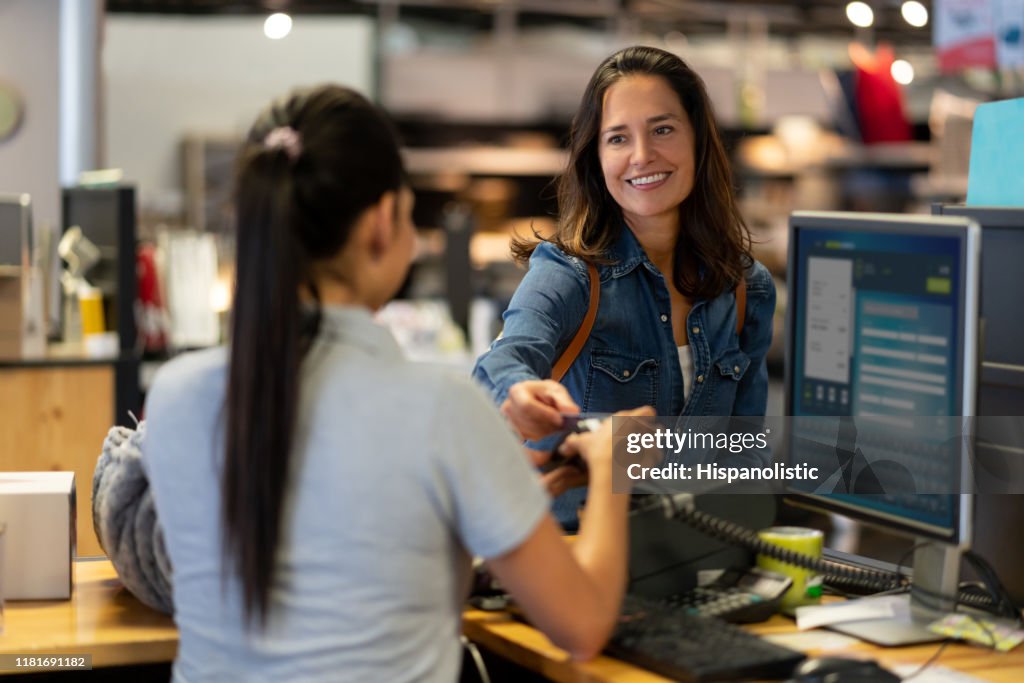Client féminin gai effectuant un paiement sans contact avec la carte de crédit à un sourire de magasin de meubles