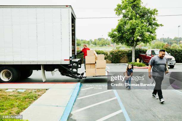 young daughter helping to carry items to moving truck while family moves - camión de las mudanzas fotografías e imágenes de stock