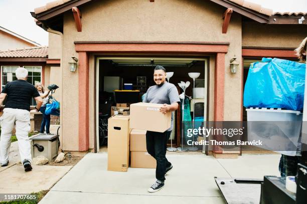 laughing man carrying box into new home on moving day - man boxes moving home stock-fotos und bilder