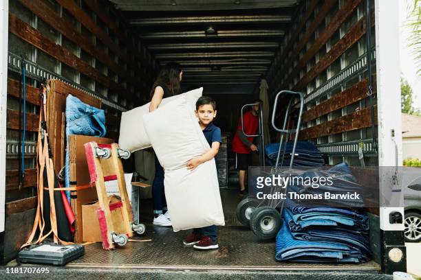 Young boy helping parents carry items from moving truck into new home